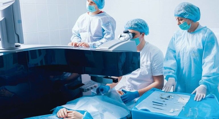 Laser_vision_correction._A_patient_and_team_of_surgeons_in_the_operating_room_during_ophthalmic_surgery._Eyelid_speculum._Lasik_treatment._Patient_under_sterile_cover