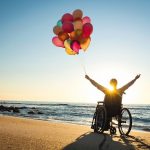 Handicapped_man_on_a_wheelchair_with_colored_balloons_at_the_beach