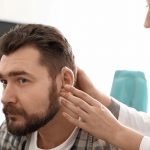 Otolaryngologist_putting_hearing_aid_in_man's_ear_in_hospital