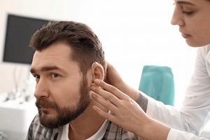 Otolaryngologist_putting_hearing_aid_in_man's_ear_in_hospital