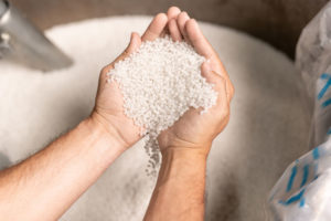 View_of_modern_factory_worker_hands_holding_pile_of_white_polymer_pellets_during_working_process