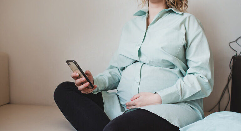 a_pregnant_girl_in_a_turquoise_shirt_holds_a_phone_in_her_hands._waiting_for_pregnancy