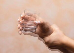 Closeup_view_on_the_shaking_hand_of_a_person_holding_drinking_glass_suffering_from_Parkinson's_disease