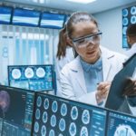 Senior_Medical_Scientist_Consults_Female_Apprentice_with_Clipboard,_He_Works_with_CT_Brain_Scan_Images_on_a_Personal_Computer_in_Laboratory._Neurologists_in_Research_Center_Work_on_Brain_Tumor_Cure.